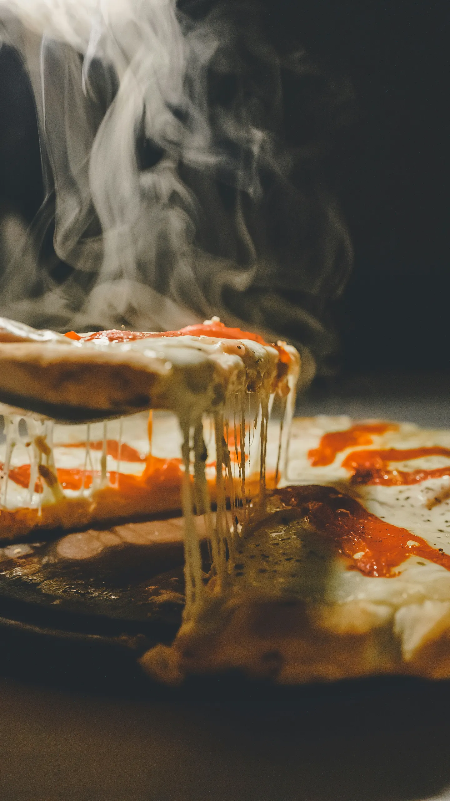 Gorąca pizza z ciągnącym się serem i parą unoszącą się nad kawałkiem